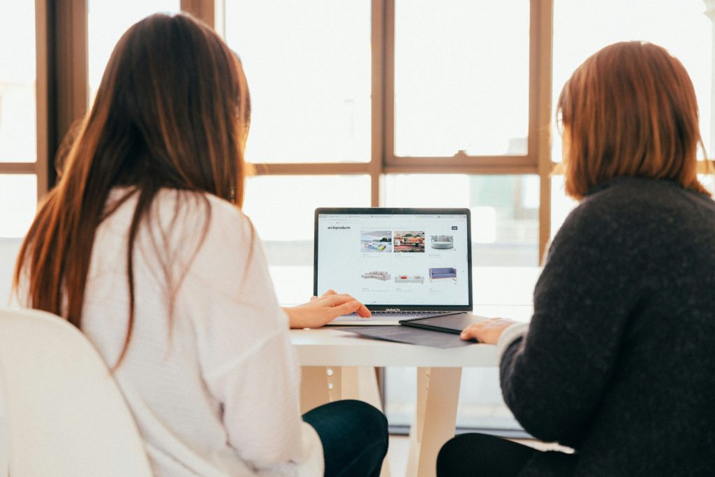 Two women talking while looking at a laptop computer.