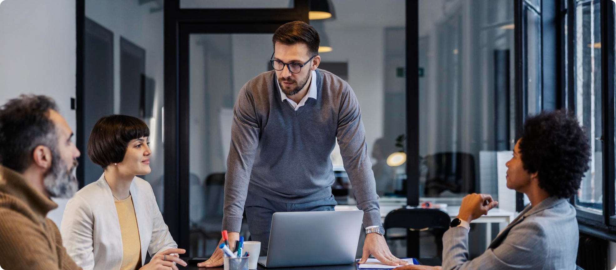 Smodin's image of a man in glasses leaning over a table in a conference room speaking to his team during a business meeting.